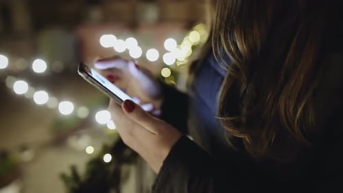 Close up of girl hands holding modern smart phone, woman's hand using cellphone at night city.