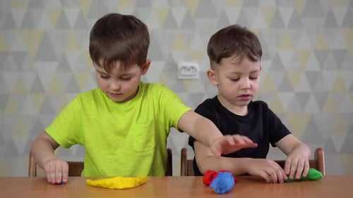 Two Boys Play with Colorful Modeling Clay at Table