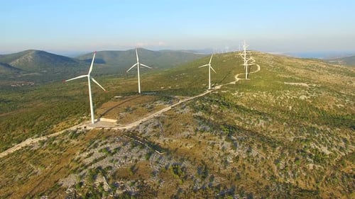 Flying above elegant ecological wind turbines on green hills