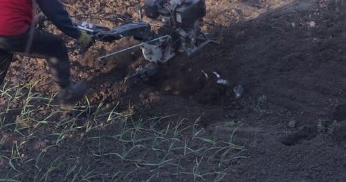 Farmer Cultivating Soil with Tiller in Rural Field