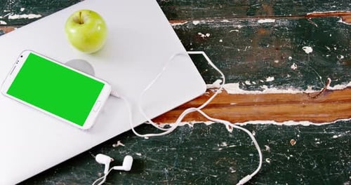Mobile phone and green apple on laptop