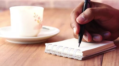 Close Up of Writing in Notebook Beside Coffee