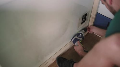 Close up shot of male person working with boring machine on wooden construction at home