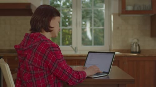 Side View of Woman Working From Home Using Laptop in the Kitchen