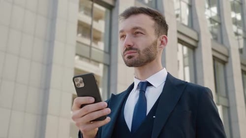 Portrait of Attractive Businessman Using Smartphone Standing at Downtown Near Modern Office Building