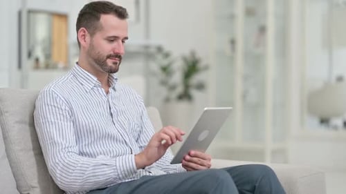 Man Uses Tablet on Sofa at Home