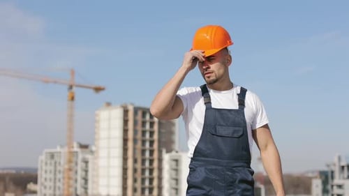Der junge Ingenieur setzt sich einen Schutzhelm auf und schaut in die Kamera