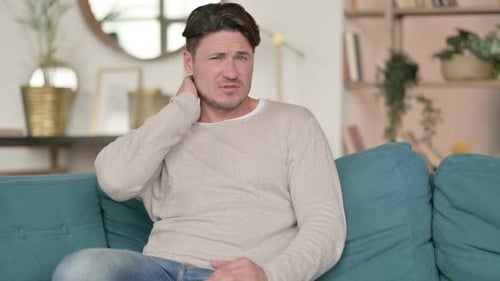 Man Rubbing Neck in Pain on Sofa