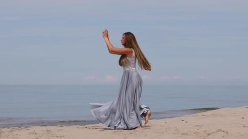 Cute Young Woman in a Long Dress Dancing on The Beach
