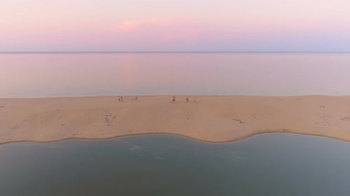Group of People Walking on Sand Stripe at Sea Coast Against Flat Sea Horizon at Sunset with Pink