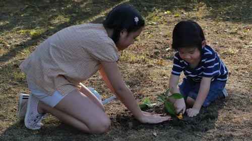 Young Adult and Child Planting Sapling in Garden
