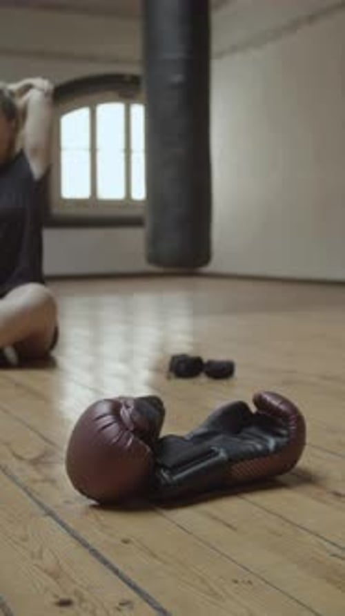 Woman Stretching Near Boxing Gloves on Gym Floor