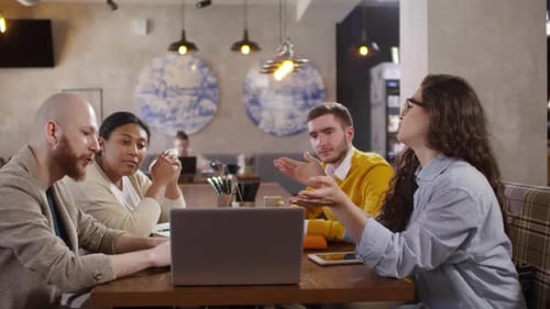 Diverse Business Team Discussing Project on Laptop in Cafe
