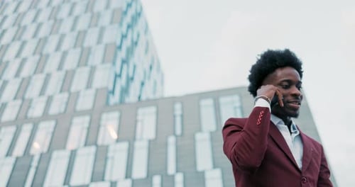 Serious Darkskinned Businessman Dressed in Suit is Standing Outside in Front of Glass Building of