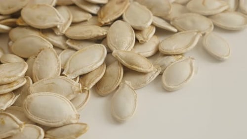 Panning over pile of pumpkin seed on white 4K 2160p 30fps UltraHD footage - Close-up of raw organic