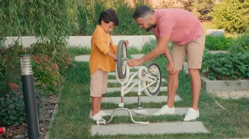 Dad Helping Child Repairing Bicycle Outdoors