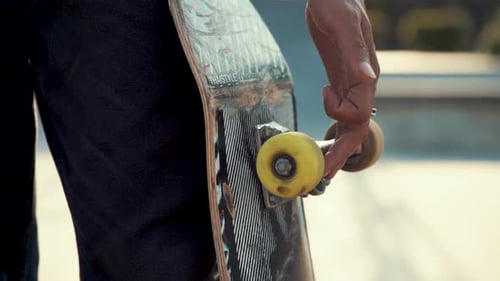 Adult Holds Skateboard with Yellow Wheels in Skatepark