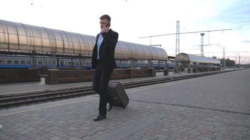 Handsome Businessman Walking Through Railway Station with His Luggage and Talking on Phone