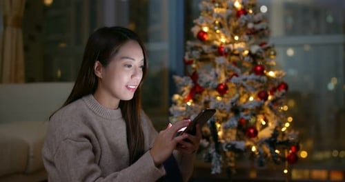Woman Using Smartphone at Night With Christmas Tree