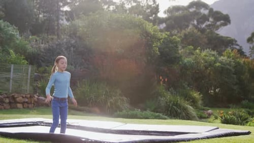 Girl Jumping on Trampoline in Backyard