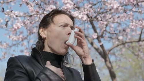 Woman Uses Inhaler Outdoors by Flowering Tree