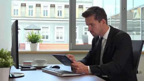 An office worker in a suit works on a computer and a tablet