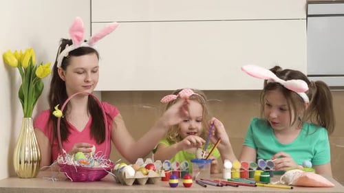 Tres hermosas chicas con orejas de conejo pintan huevos de Pascua con pintura