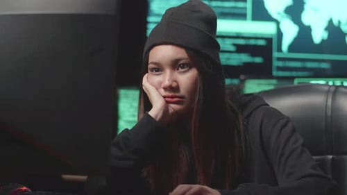 Une jeune femme asiatique qui s'ennuie utilise le piratage informatique et code sur plusieurs écrans d'ordinateur
