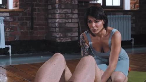 A Couple Training in the Gym Man Pumping His Abs While the Beautiful Girlfriend Holding His Feet and