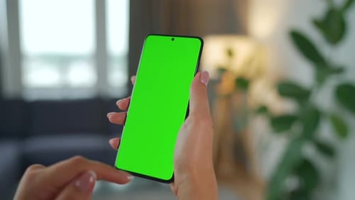 Woman at Home Using Smartphone with Green Mockup Screen in Vertical Mode