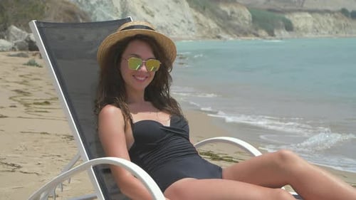 Beautiful Smiling Brunette Female Lying on the Deck Chair on the Beach