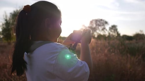 Girl standing in meadow and taking a picture by camera