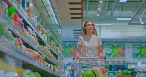 Beautiful Girl Walks Through a Supermarket with a Grocery Cart