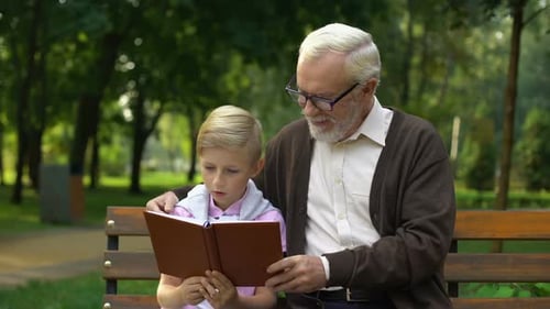 Grandfather and Grandson Reading a Book in Park