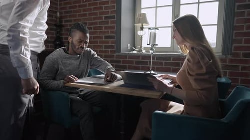 Thoughtful Young Couple Sitting in Restaurant As Waiter Serving Clients