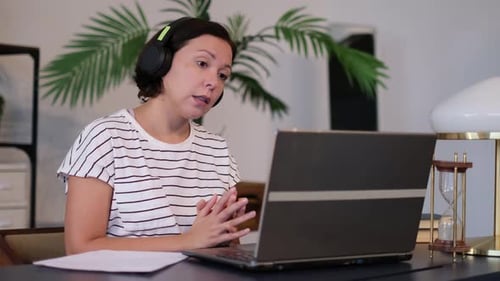 Une jeune femme porte un casque pour une conférence téléphonique sur un ordinateur portable et discute avec un enseignant en ligne qui étudie et travaille