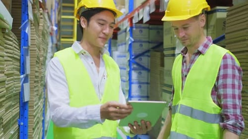 Group of diversity male workers wearing safety work helmet and vest working in industrial warehouse.
