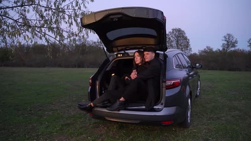 Couple Embracing in Car Trunk in Grassy Field