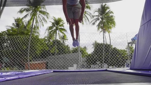 Young Man Jumps on Trampoline in Tropical Setting