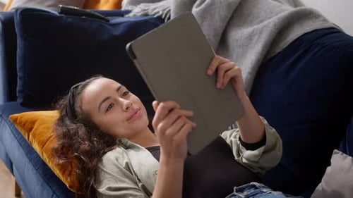 Overhead-Aufnahme einer jungen Frau, die sich zu Hause auf dem Sofa entspannt und Buch auf digitalem Tablet liest