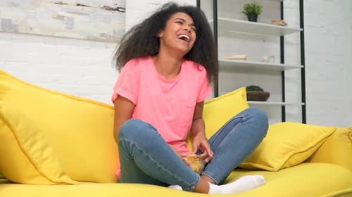 Young Woman Laughing Watching TV on Yellow Couch