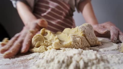 Hands Kneading Dough on Floury Wooden Table