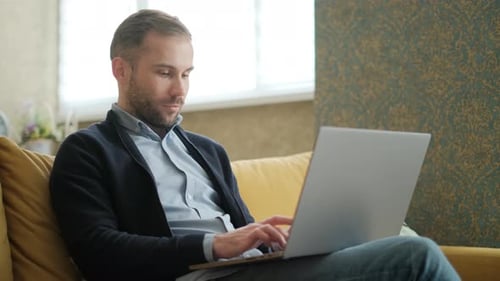 Man Using Laptop on a Couch Indoors
