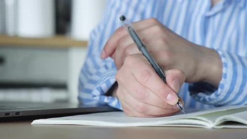 Close Up Of A Woman's Hand Holding A Pen And Writing Notes In A Notebook Sitting At Home