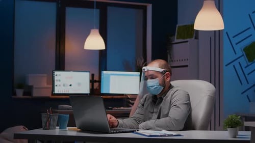 Homme d'affaires bourreau de travail avec masque facial et visière contre Covid19 travaillant au bureau de l'entreprise