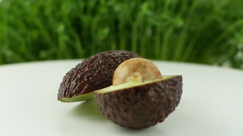 Avocado rotates on a green grass background. Avocado with a bone in a cut, rotating in slow motion.