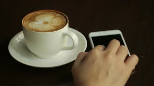 Hand Using Cellphone Next to Coffee Cup