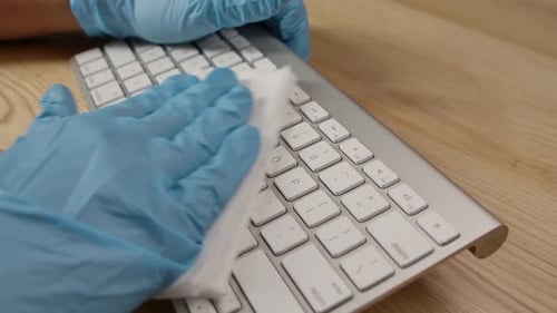 Person's Hand in Blue Protective Medical Glove Using Wet Wipe and Cleaning Carefully Laptop Keypad