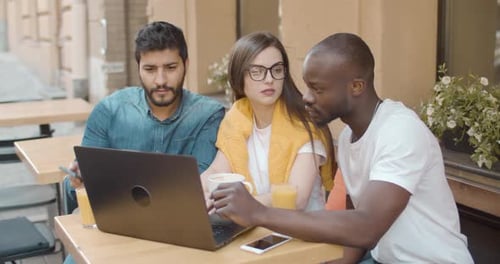 Three Young Adults Collaborate at Outdoor Cafe