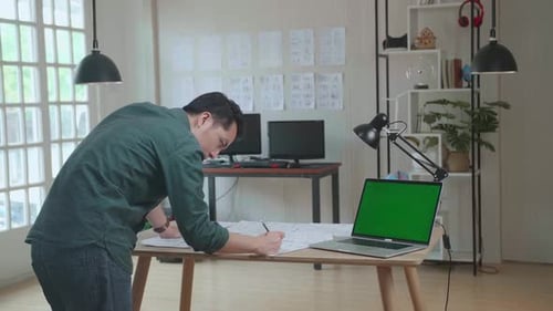 Asian Man Drawing Storyboard Animation Comic Cartoon With Mock Up Green Screen Laptop Computer